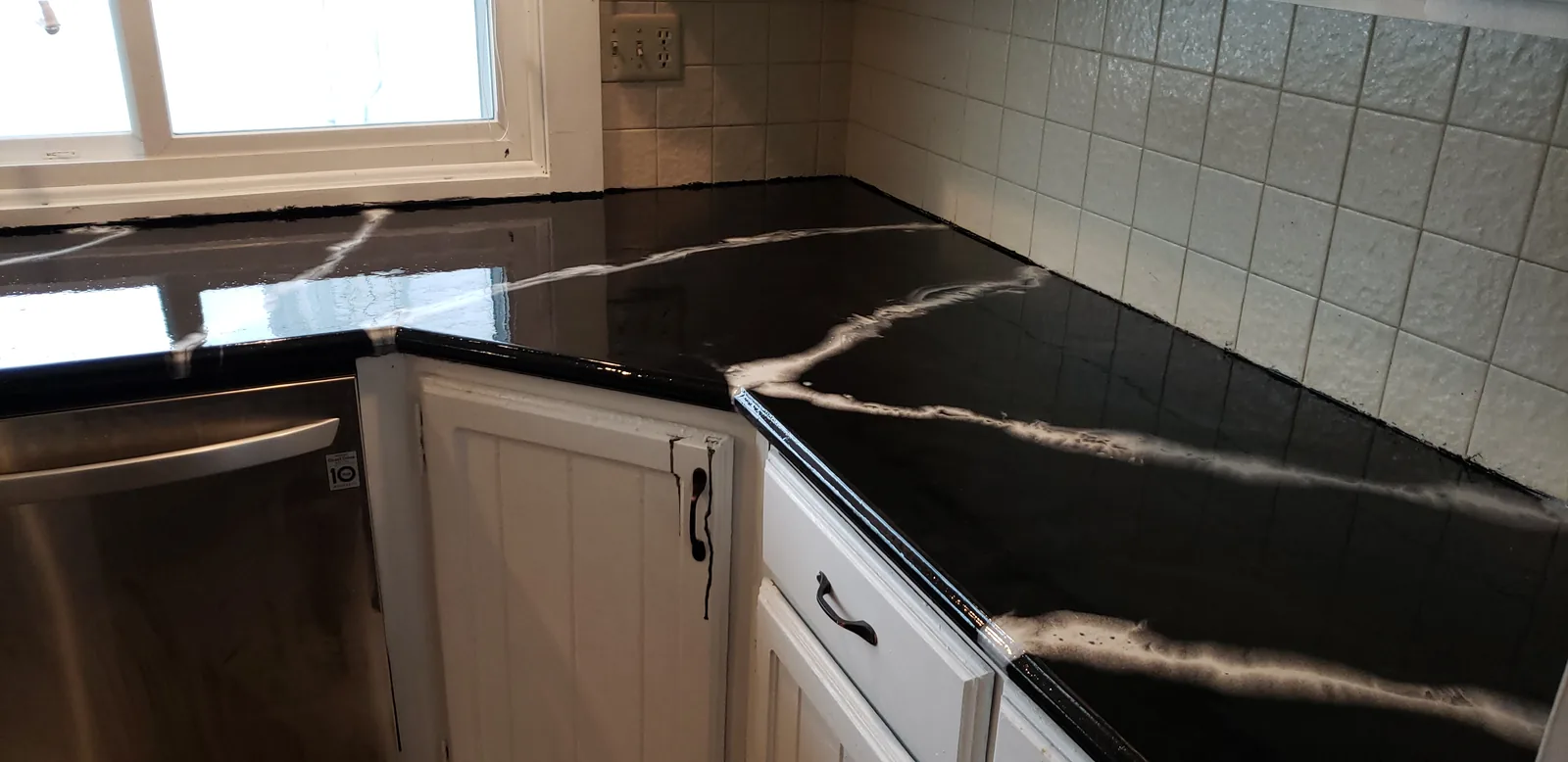 Epoxy restored kitchen countertop in a black marble look by the dishwasher by DC Coatings, Green Bay, WI